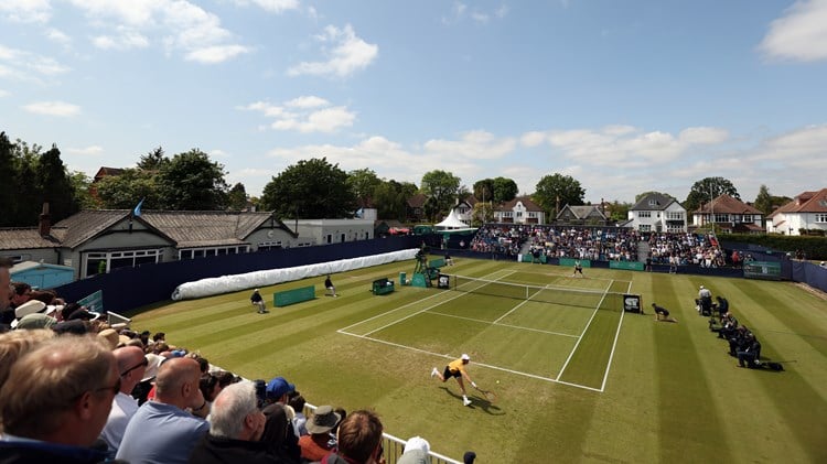 A view of a game being played on a grass court at Surbiton Trophy with crowds watching. 