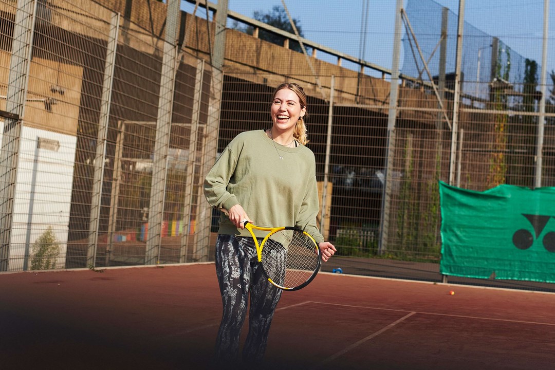 Woman laughing on tennis court holding racket