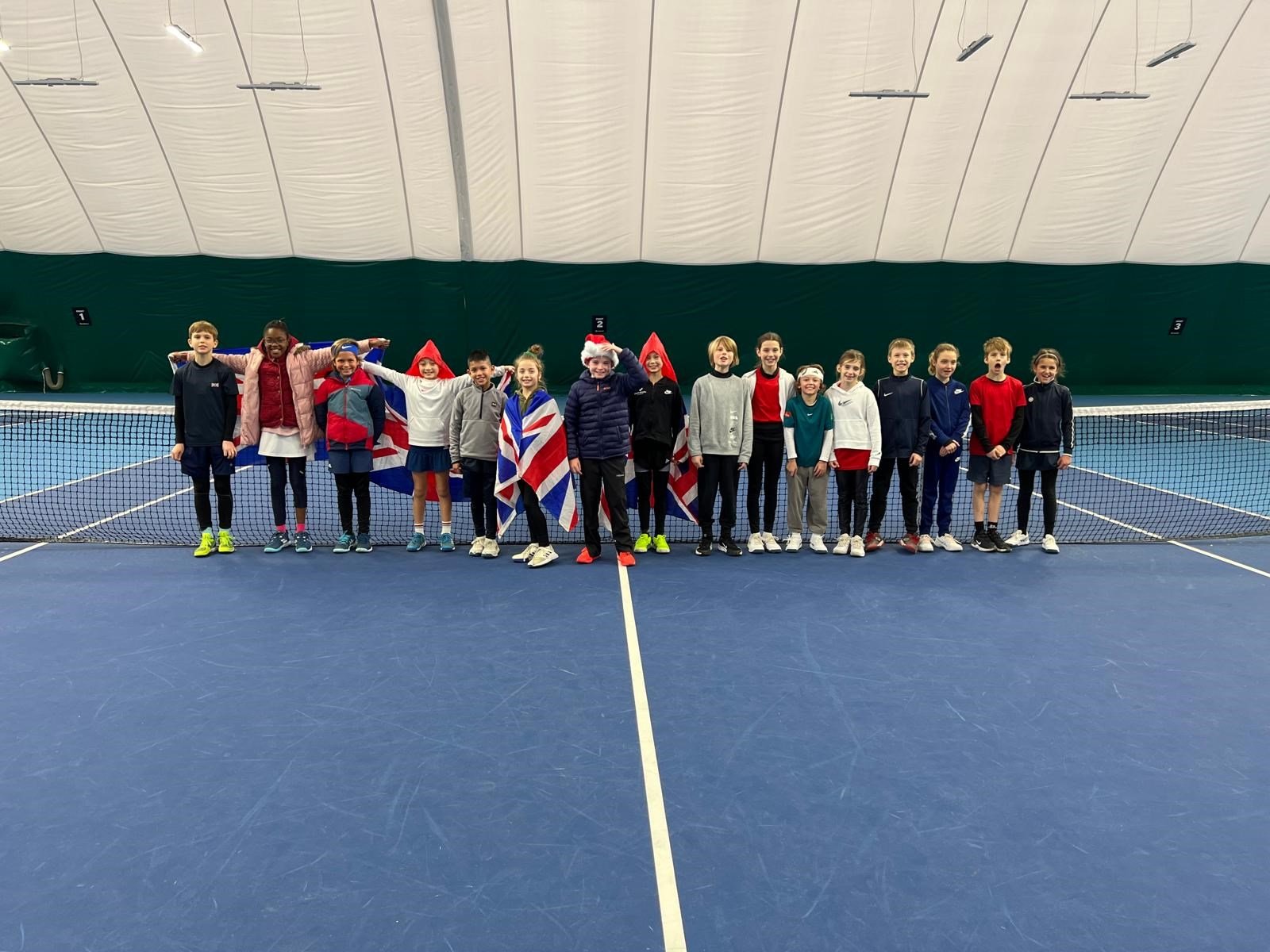 Children posing by the net on a tennis court after a 11U and 12U matchplay session