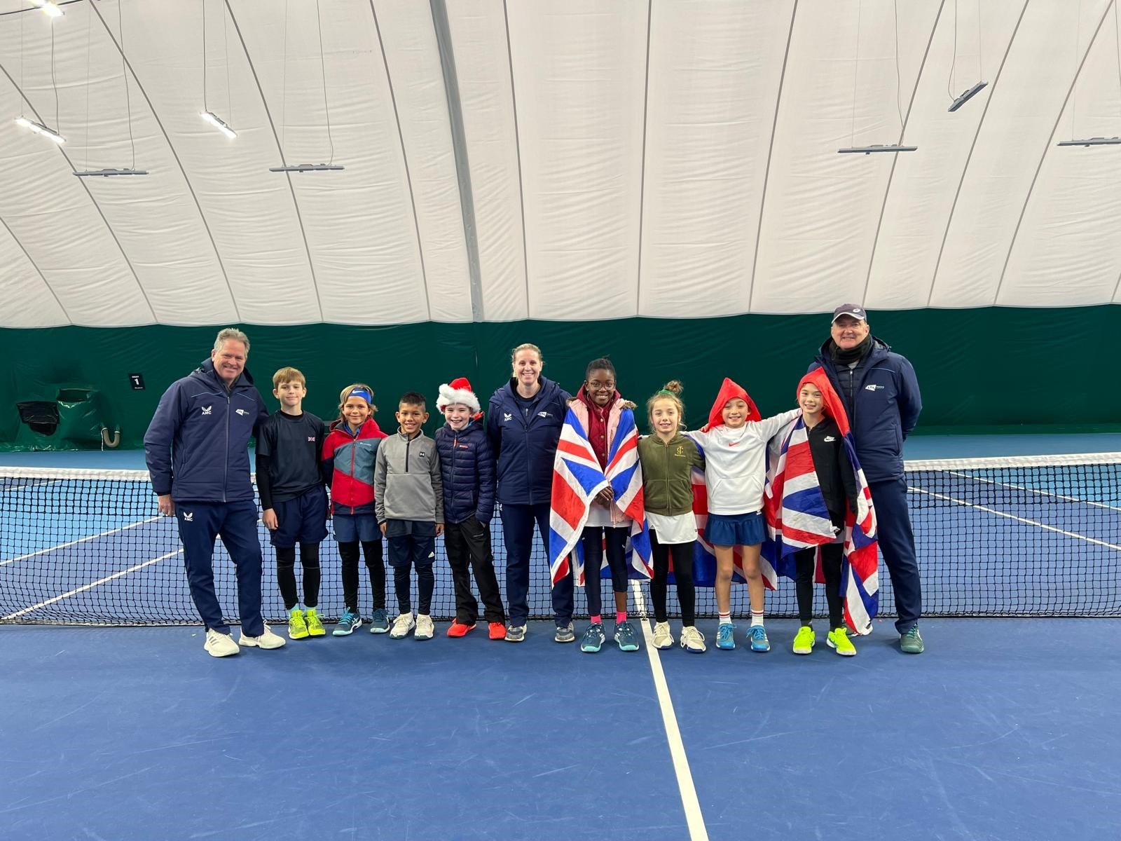 11U and 12U players posing by the net on a tennis court with their LTA coaches