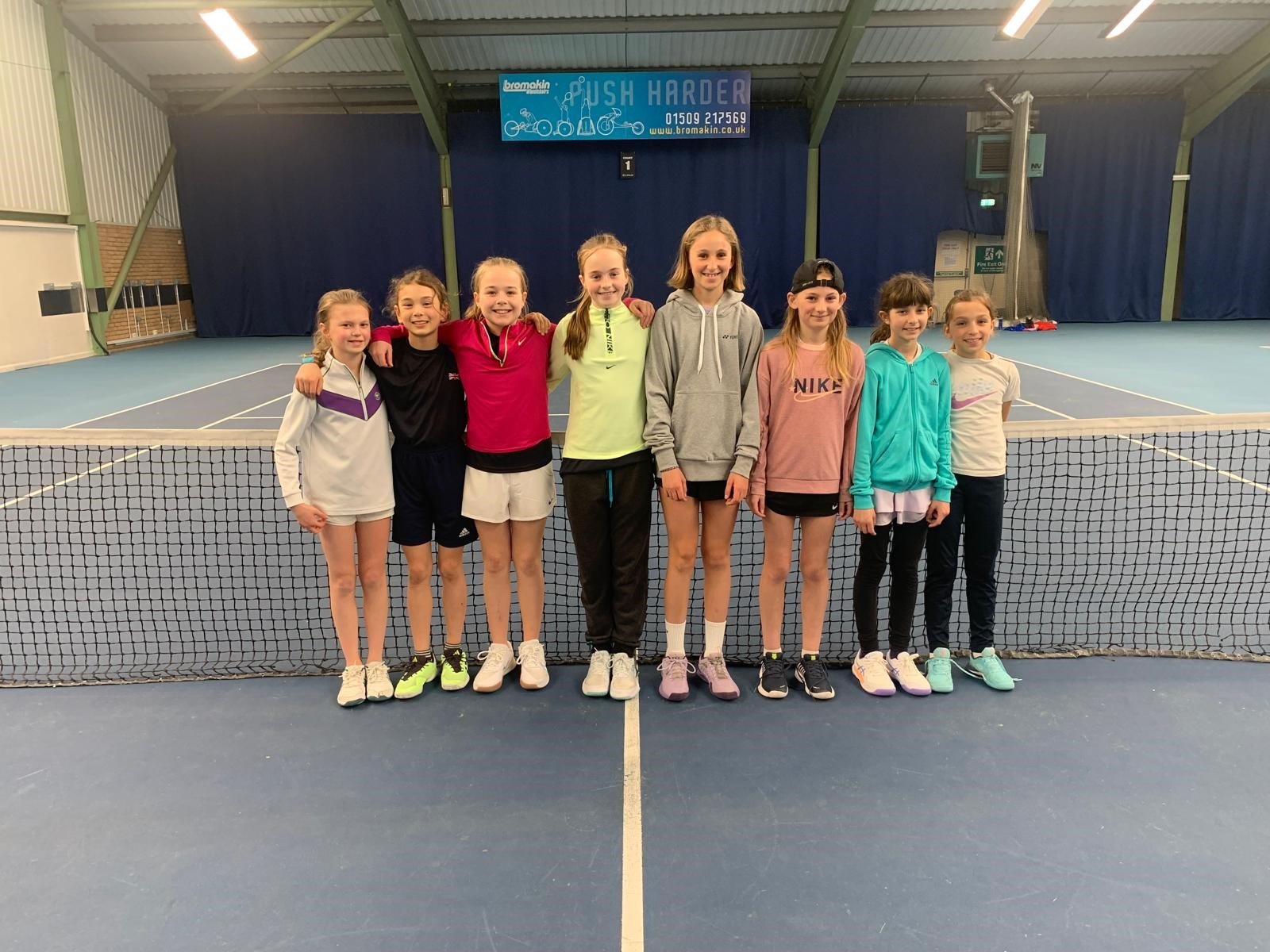 A group of young female players posing by the net after a U12 matchplay session