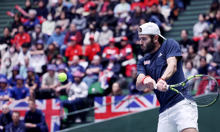 Jacob Fearnley preparing to hit a backhand at the Davis Cup with multiple Great Britain flags in the background