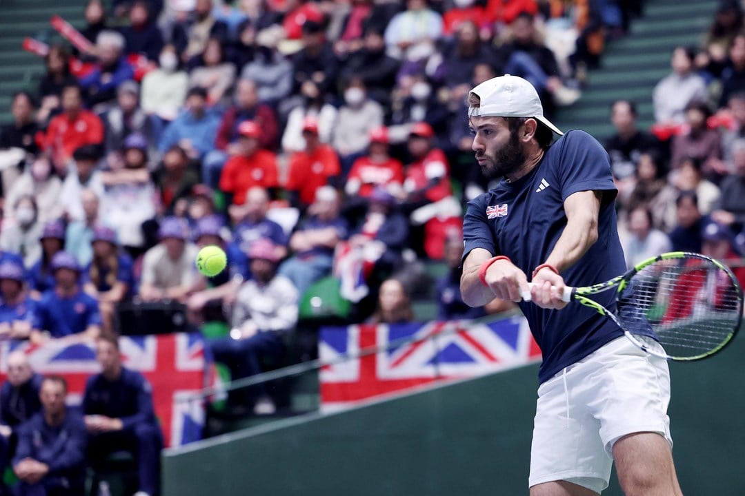 Jacob Fearnley preparing to hit a backhand at the Davis Cup with multiple Great Britain flags in the background