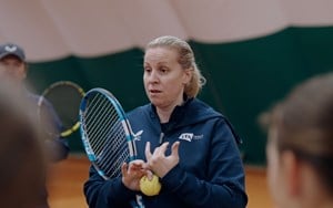 Coach Hollie Bainbridge chatting through a exercise with a racket and ball in hand