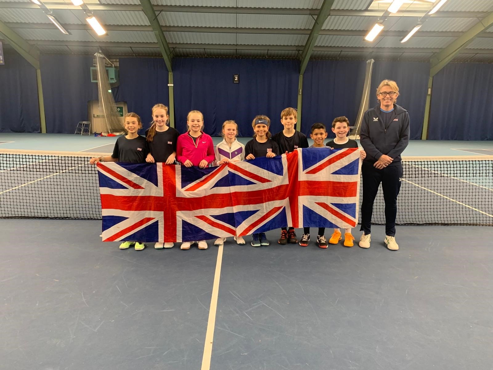 A group of eight U12 players posing with Union Jacks and their coach in front of the net