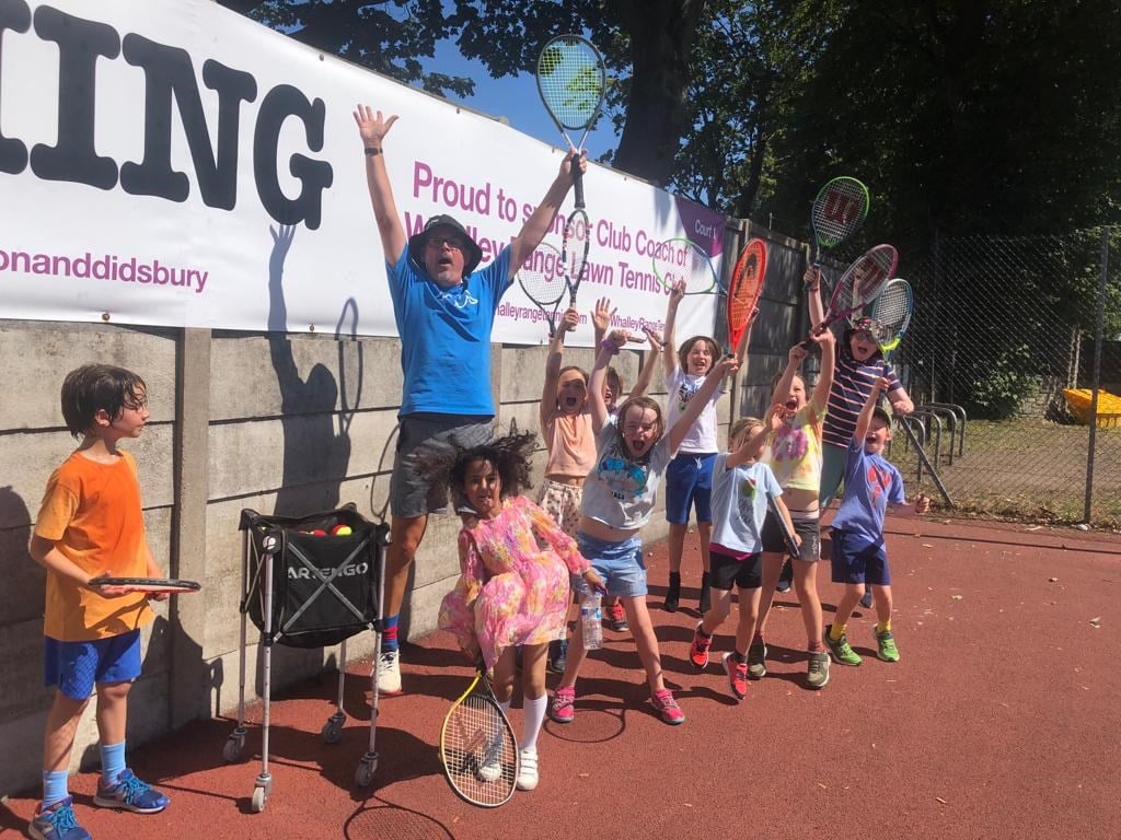Head Coach of Whalley Tennis Club, Simon Wood, celebrating with the kids from his youth sessions while they wave their rackets in the air.