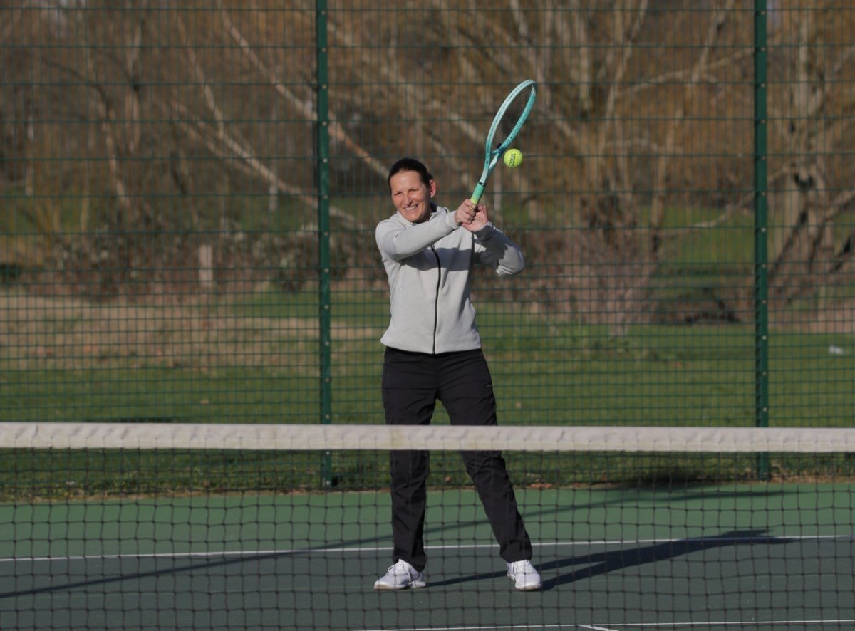 On a tennis court, a woman grips her tennis racket, poised for action and focused on the game.