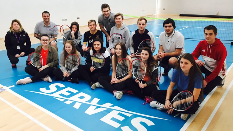 SERVES session group posing with rackets, seated on the floor besides Serves logo at Leigh park