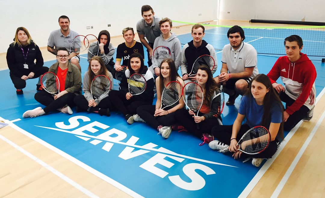 SERVES session group posing with rackets, seated on the floor besides Serves logo at Leigh park