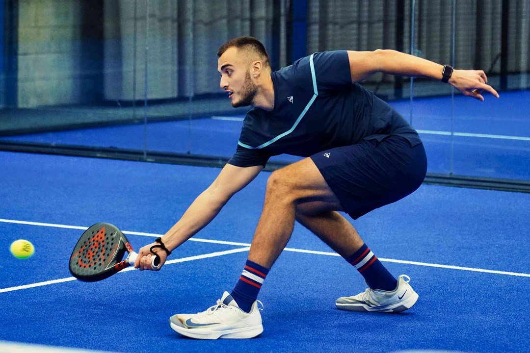 Louie Harris bending down to retrieve a ball with his padel bat on court