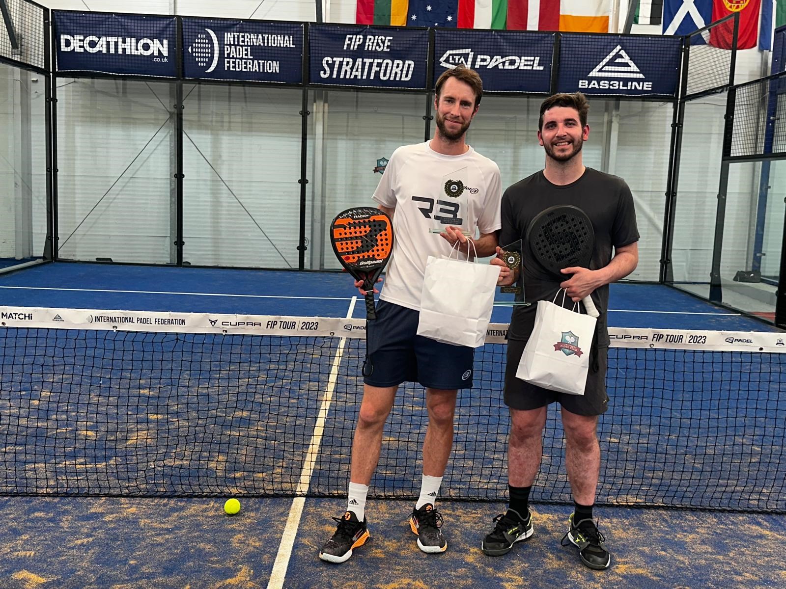 Chris Salisbury and Alfonso Patacho holding their trophies and padel bats on court at the FIP Rise event in Stratford
