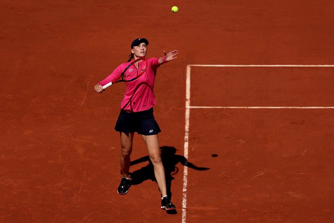 Elena Rybakina stood on a clay court while throwing a tennis ball in the air as she prepares to serve