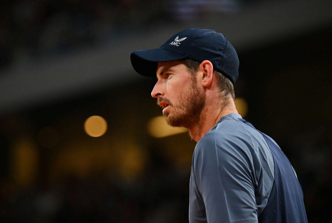 Andy Murray stood staring ahead on court while wearing a baseball cap