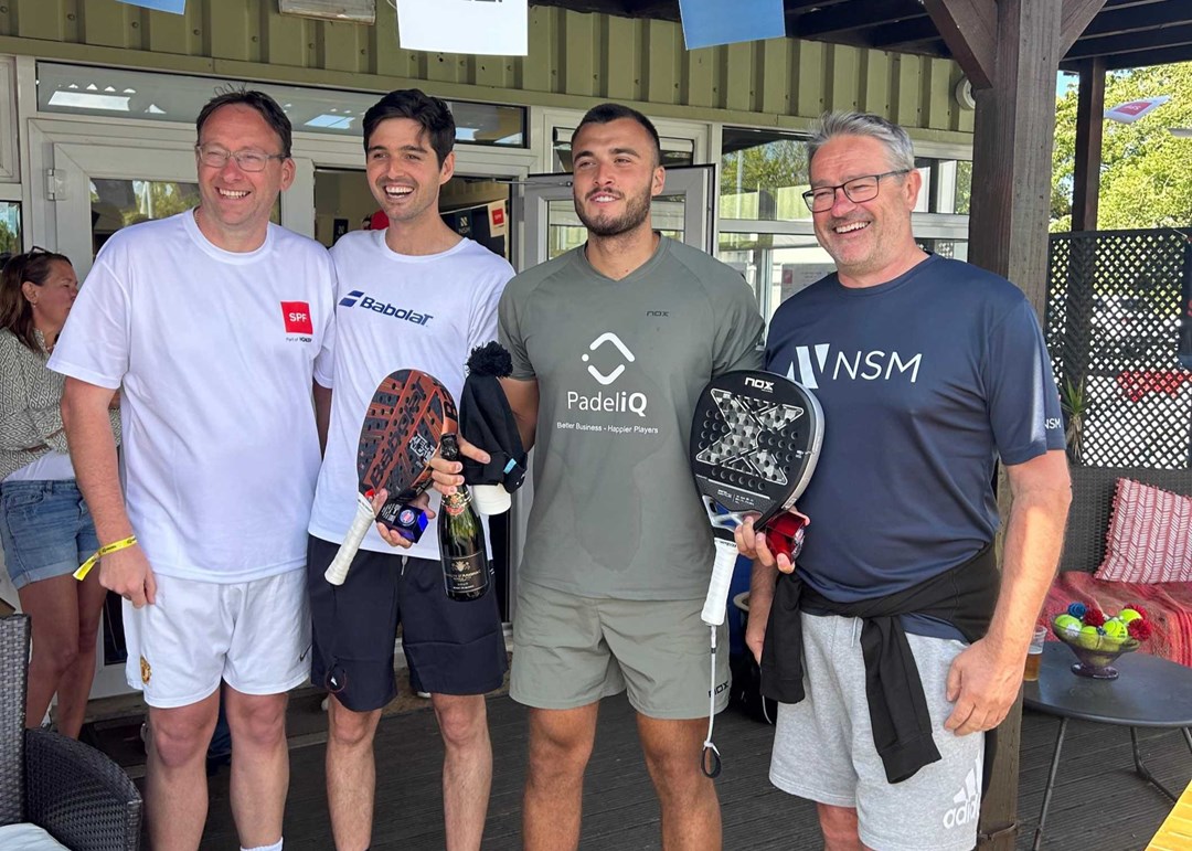 Louie Harris and Rafael Vega holding their padel bats, a bottle of champagne and their trophies alongside two men at the Padel British Tour event in Guernsey