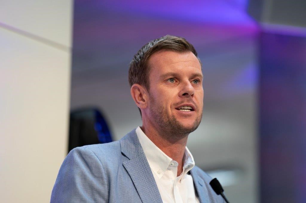 Leon Smith speaking into a microphone wearing a blue blazer jacket