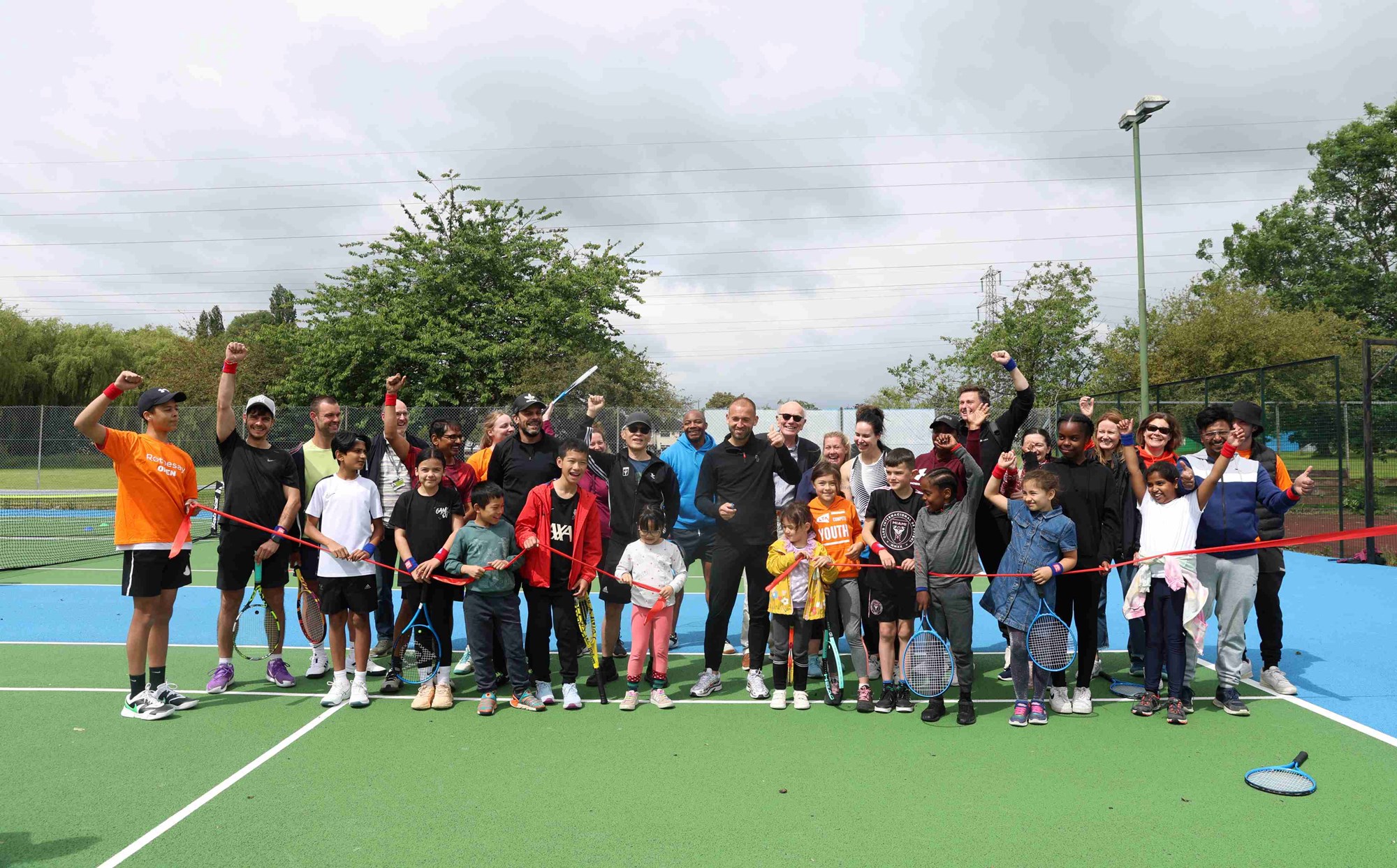 British tennis star Dan Evans surrounded by adults and children on a park tennis court after a Free Parks Tennis session
