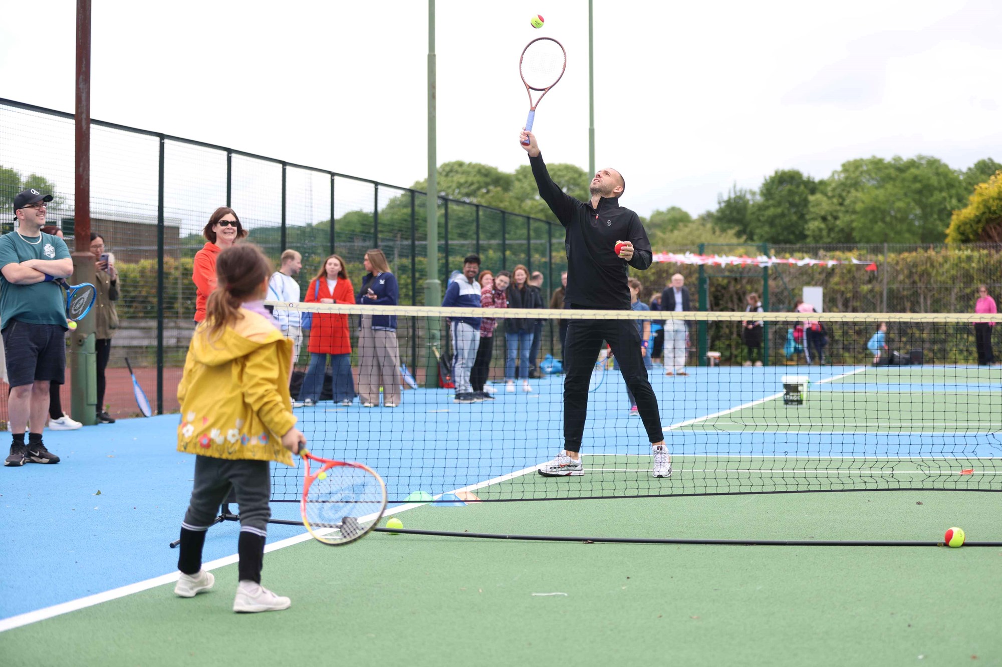 Dan Evans playing tennis with a young girl on a park tennis court