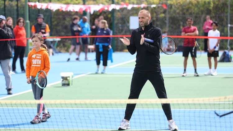 Dan Evans stood on court next to a young girl with an LTA Youth jumper playing tennis