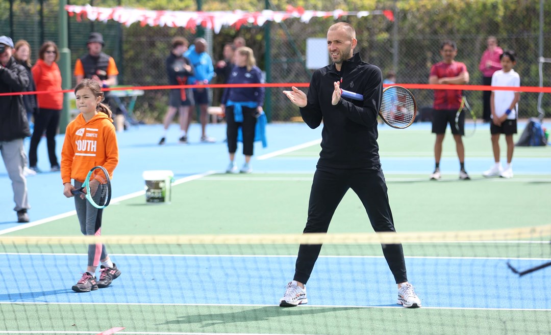 Dan Evans stood on court next to a young girl with an LTA Youth jumper playing tennis