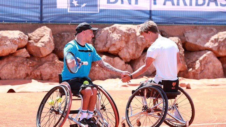 Andy Lapthorne and Niels Vink sat in their wheelchairs holding tennis rackets and shaking hands on court