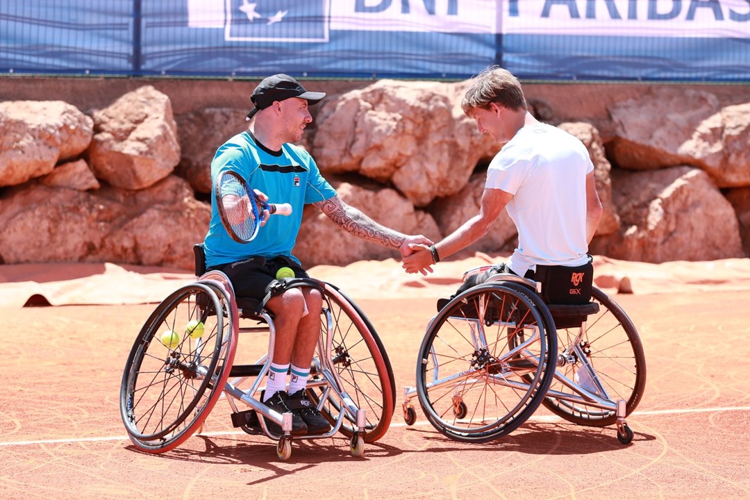 Andy Lapthorne and Niels Vink sat in their wheelchairs holding tennis rackets and shaking hands on court