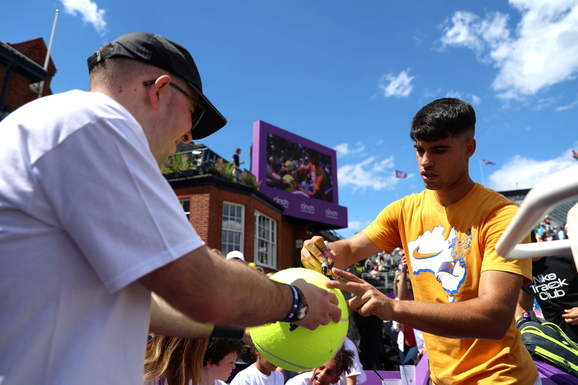 Carlos Alcaraz signing a person's giant tennis ball on court at the cinch Championships