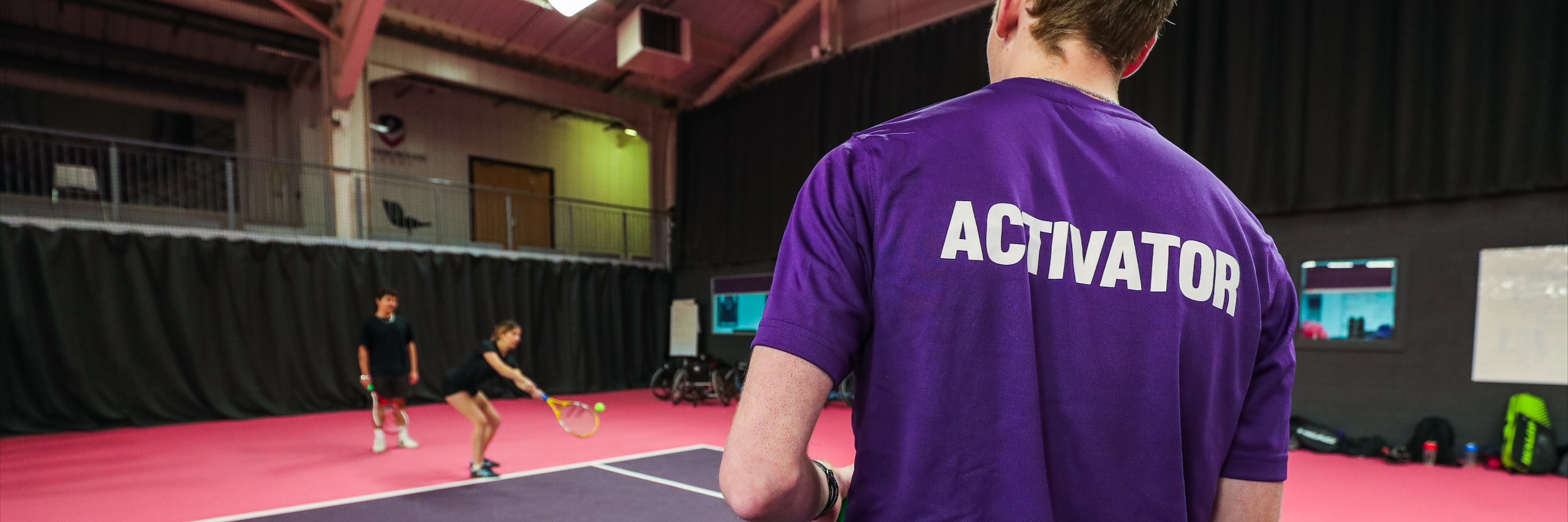 A University Activator coaching university tennis players on an indoor court