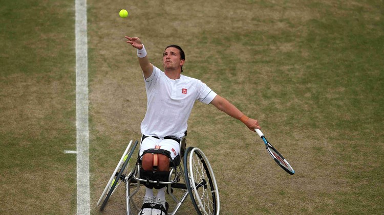 Wheelchair tennis player Gordon Reid throws tennis ball in the air and prepares to hit a serve on a grass court