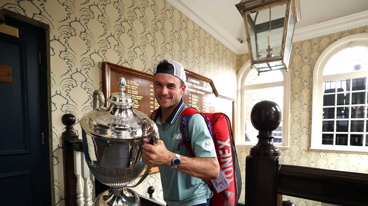 Tommy Paul walking up the stairs at the Queen's Club while carrying his trophy and smiling