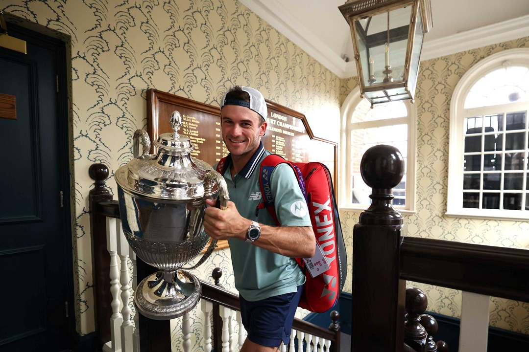 Tommy Paul walking up the stairs at the Queen's Club while carrying his trophy and smiling