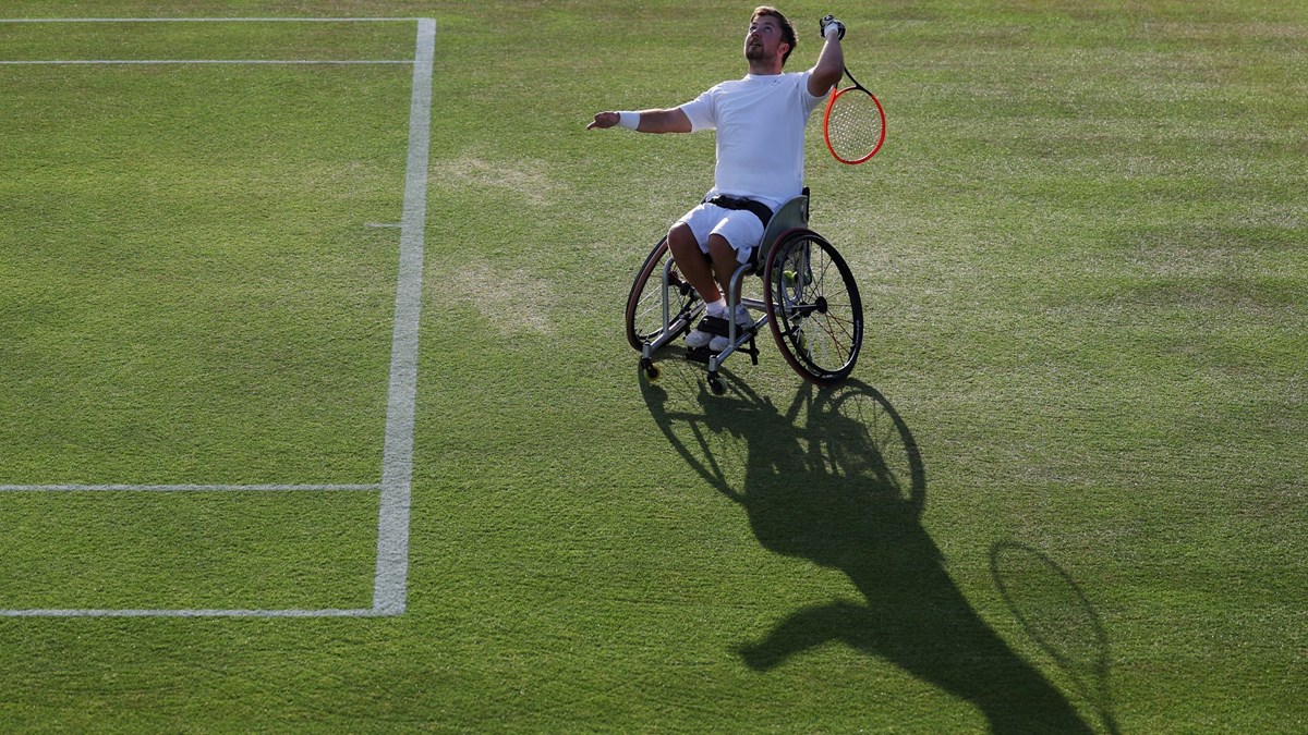 Wheelchair tennis star Sam Schroder about to hit an overheard with his shadow showing on the grass in front of him