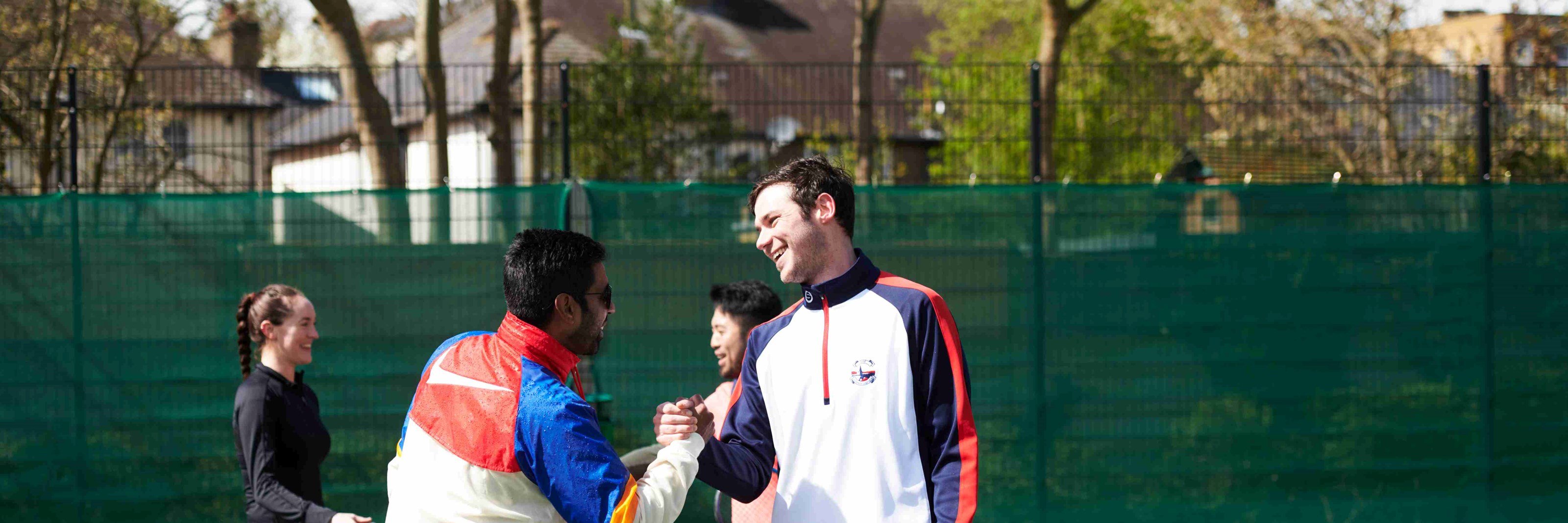 Four people on a tennis court shaking hands at the net