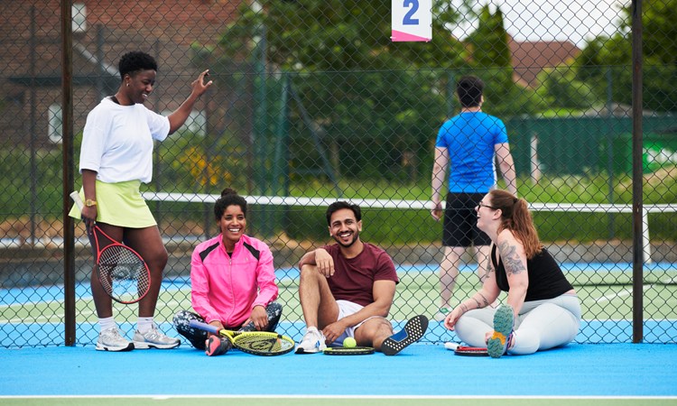 A group of people laughing together at the side of a public tennis court