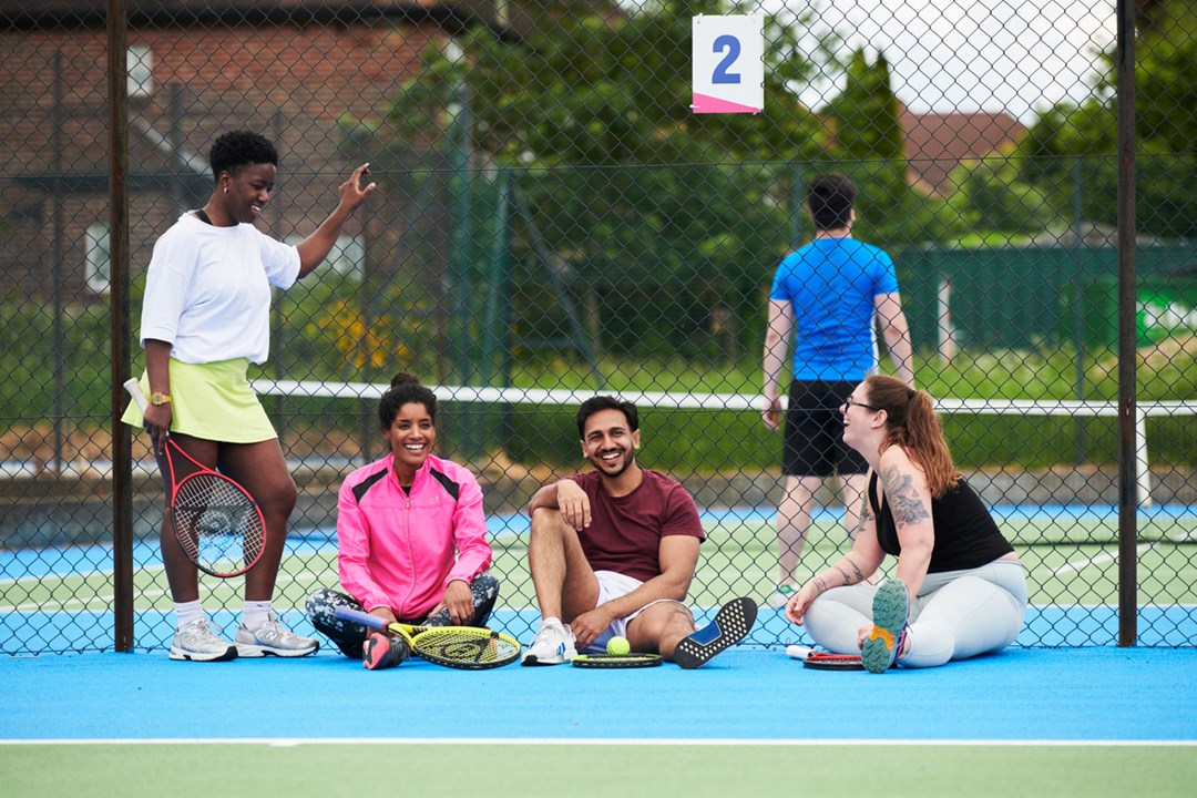 A group of people laughing together at the side of a public tennis court
