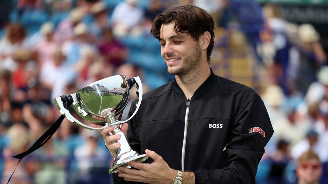 Taylor Fritz smiling and looking down at his trophy on court at the Rothesay International Eastbourne