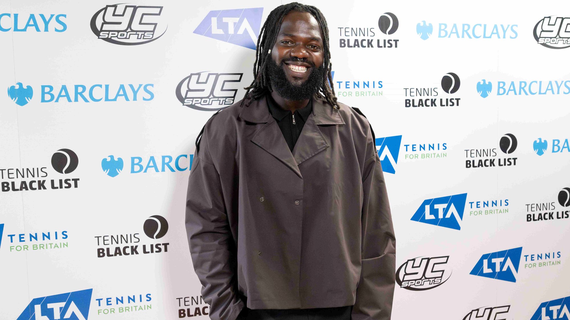 A man dressed in a grey coat smiling at the Tennis Black List Awards