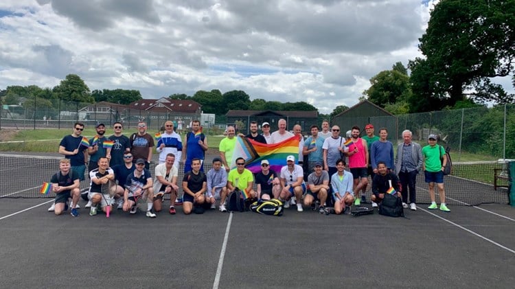 Members of the ACE Players Tennis Croydon LGBTQ+ Tennis Group pictured as group on court, holding the rainbow flag.