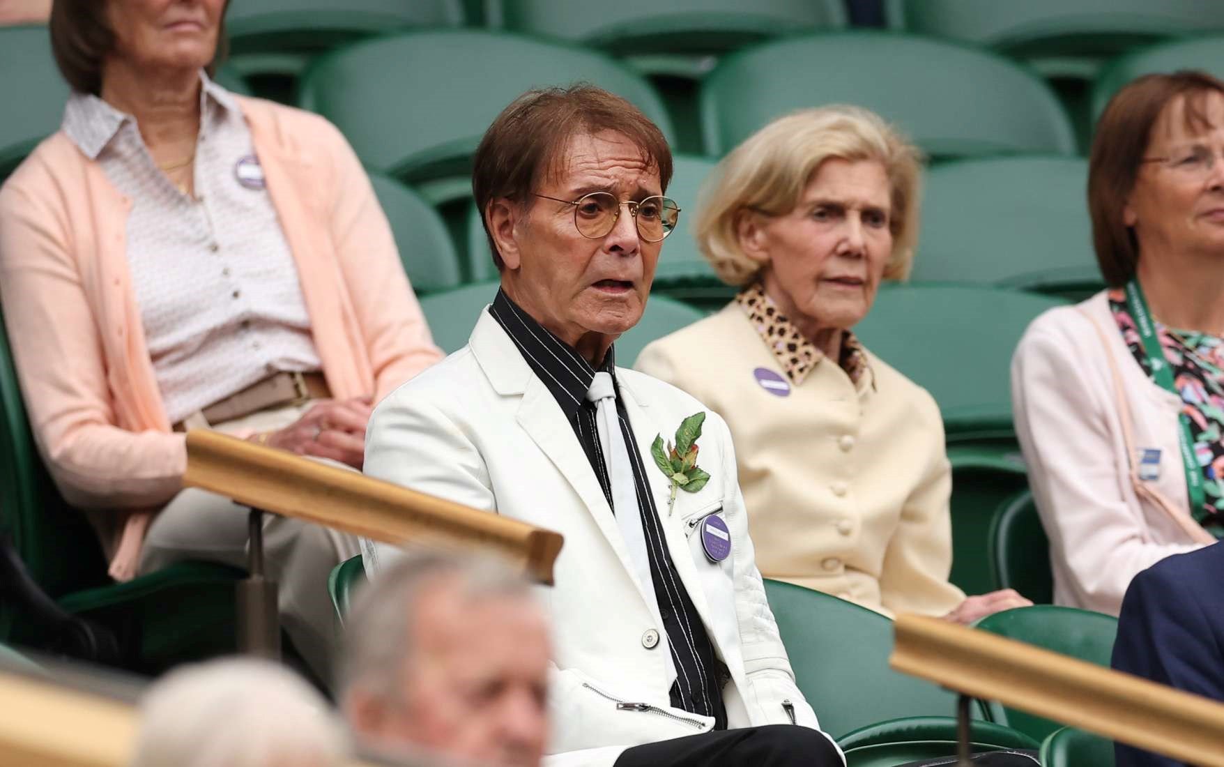 Cliff Richard wearing a white suit while looking on at Wimbledon