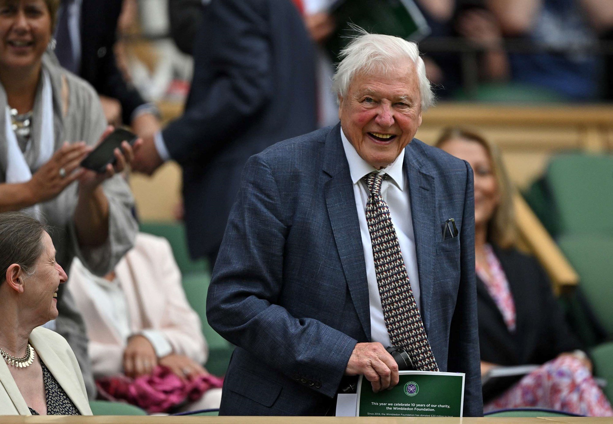 Sir David Attenborough wearing a suit and smiling in the Royal Box