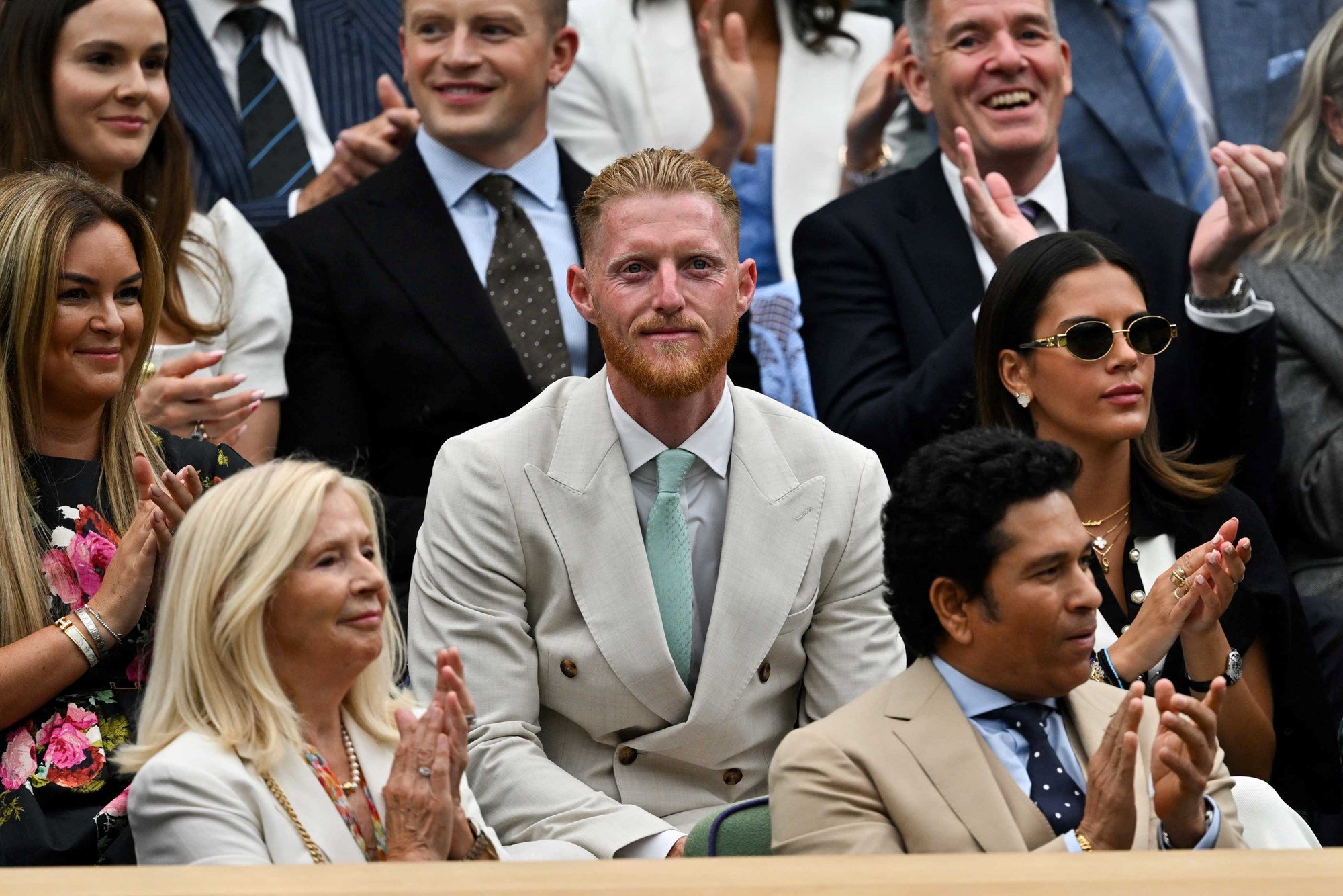 Ben Stokes wearing a suit and smiling in the crowd at Wimbledon