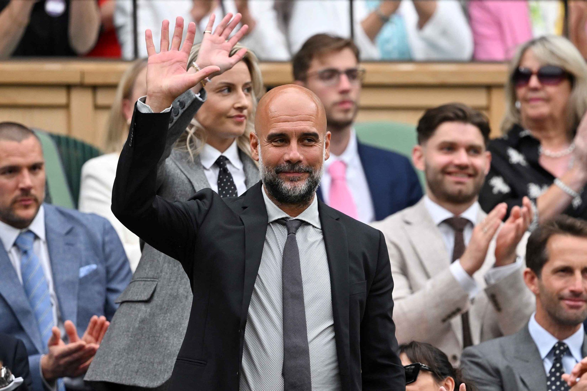 Pep Guardiola smiling while stood up and waving to the crowd at Wimbledon