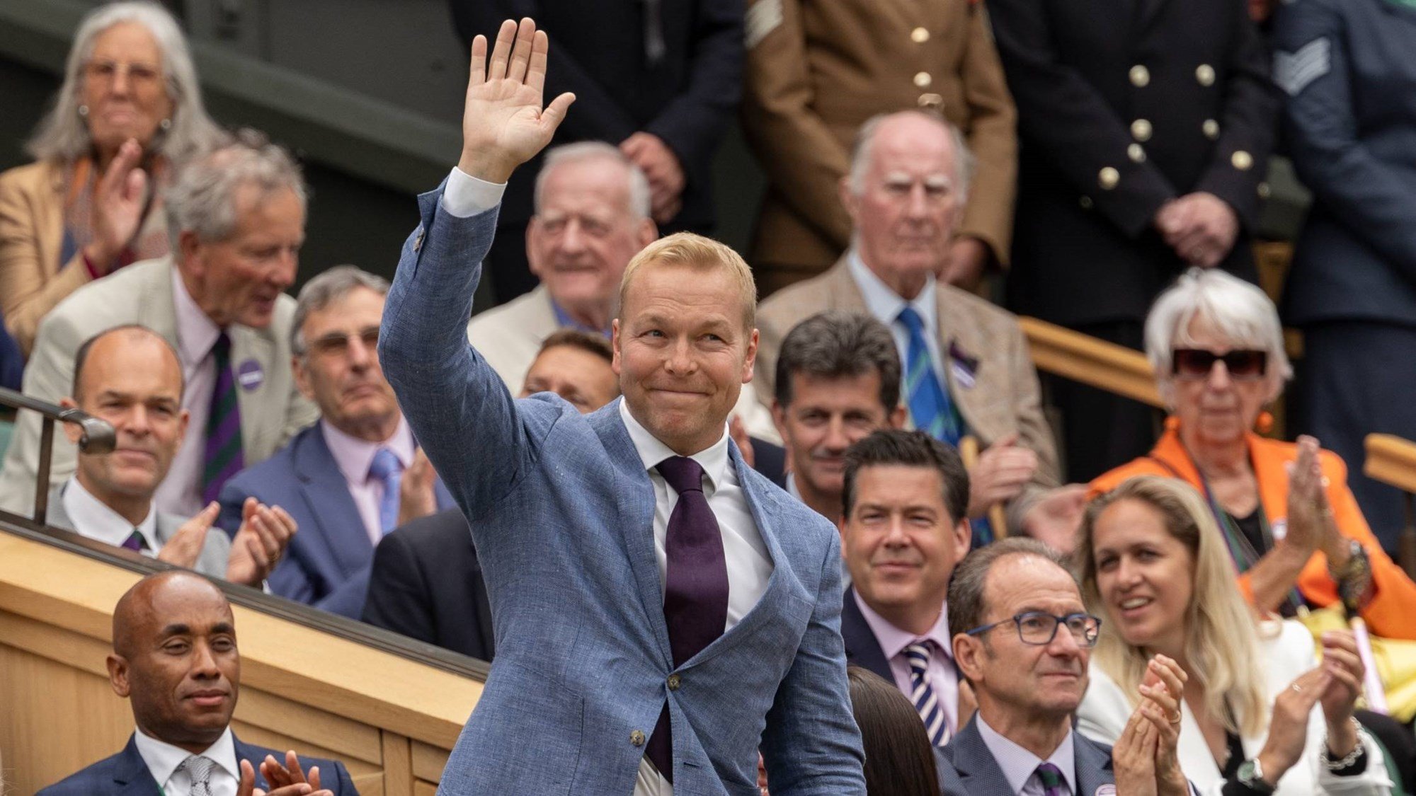 Chris Hoy smiling and waving at the crowd while wearing a suit