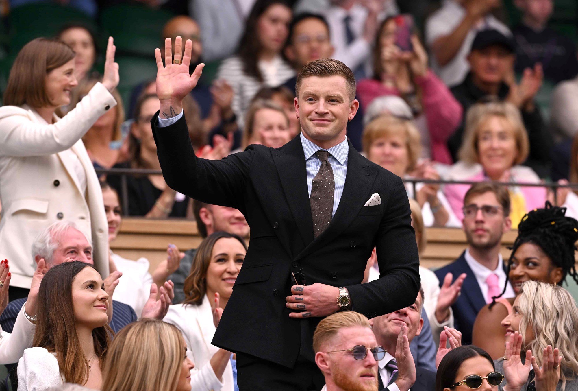 Adam Peatty, wearing a suit, while waving at the crowd at Wimbledon