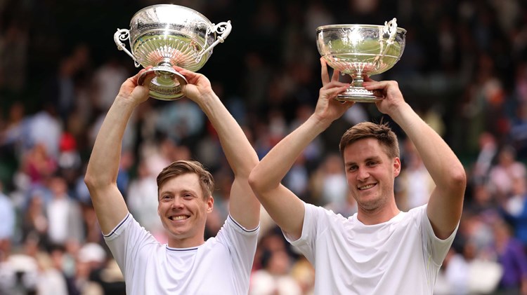Harri Heliovaara and Henry Patten holding their Wimbledon trophies above their heads while smiling