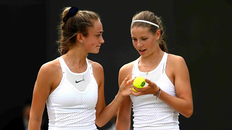 Isabelle Lacy smiling at Hannah Klugman who is holding a tennis ball on court at the Wimbledon Girls doubles final