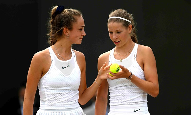 Isabelle Lacy smiling at Hannah Klugman who is holding a tennis ball on court at the Wimbledon Girls doubles final