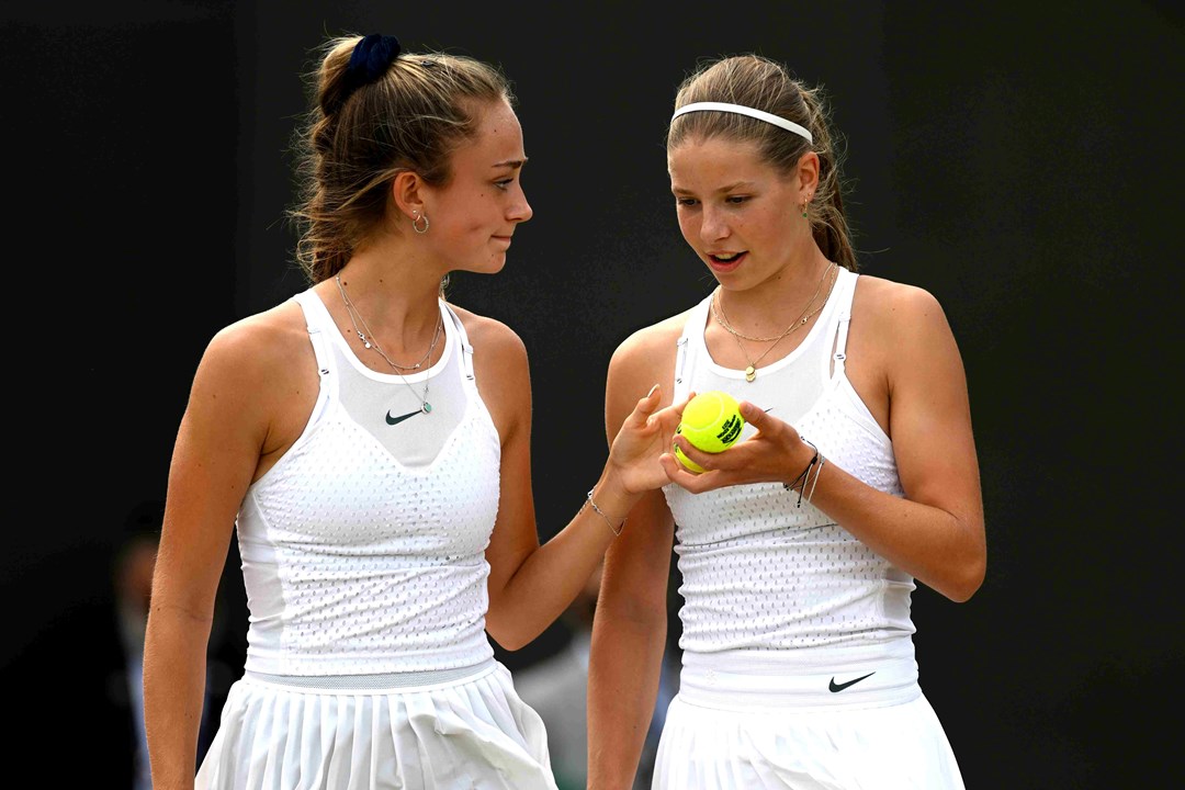 Isabelle Lacy smiling at Hannah Klugman who is holding a tennis ball on court at the Wimbledon Girls doubles final