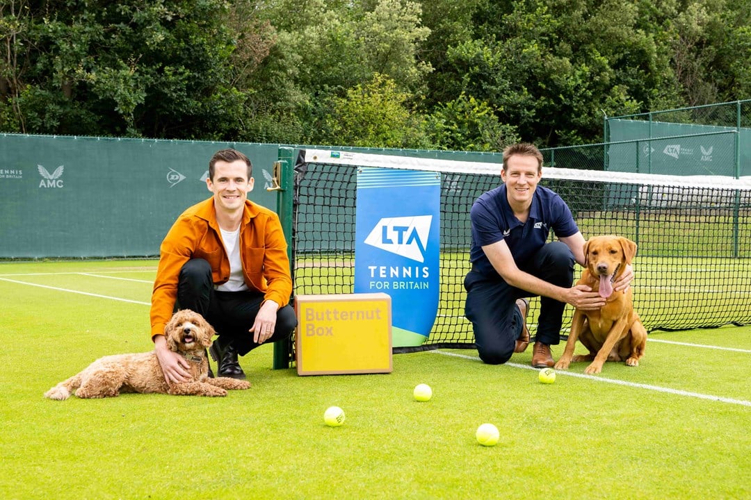 LTA partners Butternut Box on a tennis court with two dogs and a box of their freshly made dog food