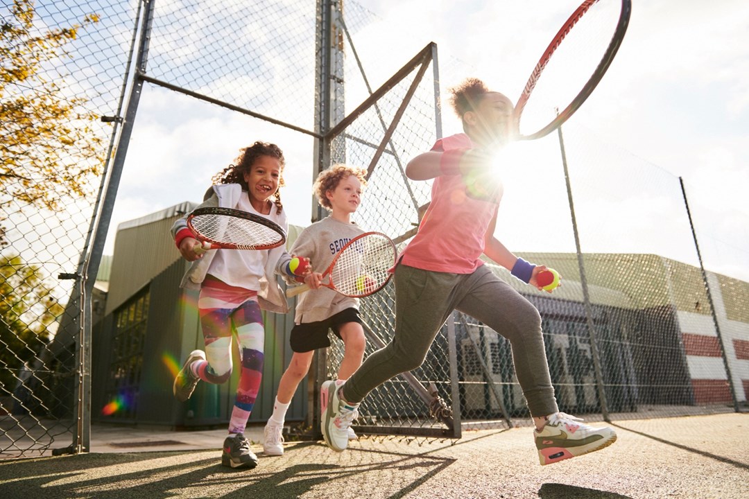 Kids running on to court with a ball and racquet in hand