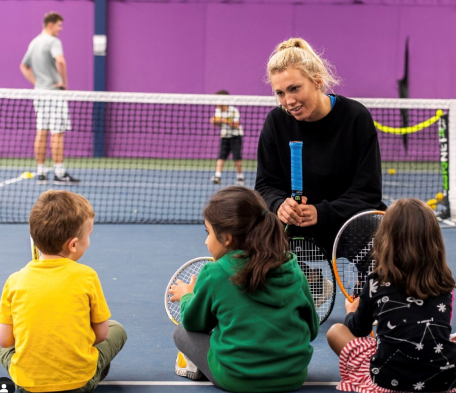 A couch kneeling down to chat to some children during a tennis session